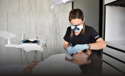 dental specialist wearing a mask, blue gloves, and magnification loupes performing an examination on a patient in a modern dental operatory