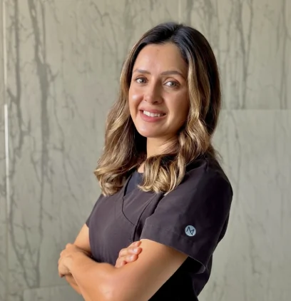 Portrait of Dr. Dulce Fragoso, a dental professional, smiling warmly with arms crossed. She wears black medical scrubs and stands in front of a grey textured marble wall