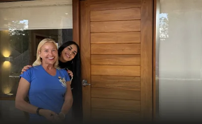 Two smiling women, a happy patient and a dental care team member, posing enthusiastically in front of the clinic's modern wooden entrance.
