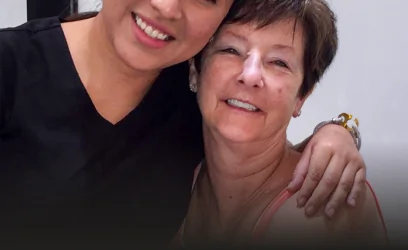 Dr. Martha Tziu wearing black scrubs, warmly hugging a smiling older female patient, highlighting a friendly and trusting doctor-patient relationship.
