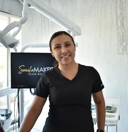 A portrait of a smiling female dental professional, Dr. Martha Tziu, wearing black scrubs in a modern dental office with marble-patterned walls.