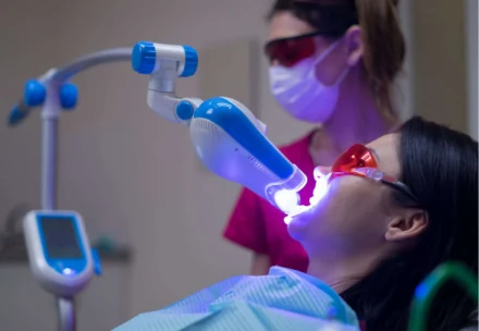 Patient wearing protective eyewear undergoing a professional laser teeth whitening procedure with a dental technician monitoring the treatment.