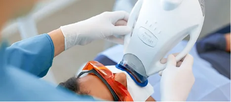 Dentist performing a Zoom whitening procedure using clinical-grade LED technology on a patient wearing protective eyewear.